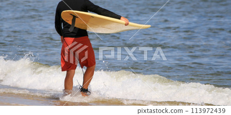 Standing at the waters edge holding a surfboard Standing at the waters edge holding a surfboard 113972439