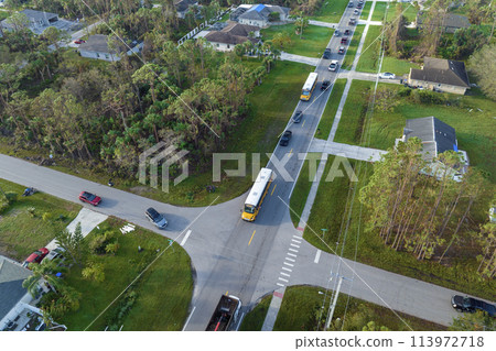 Aerial view of american yellow school bus picking up children at sidewalk bus stop for their lessongs in early morning. Public transportation in the USA 113972718