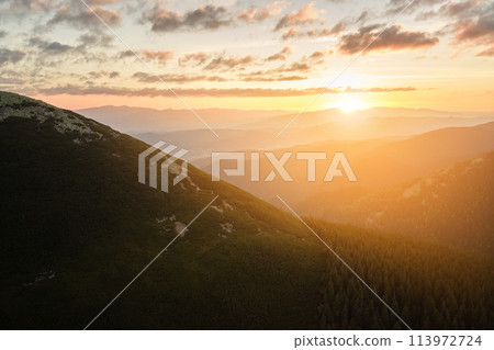 Aerial view of amazing scenery with foggy dark mountain peak covered with forest pine trees at autumn sunrise. Beautiful wild woodland with shining rays of light at dawn 113972724