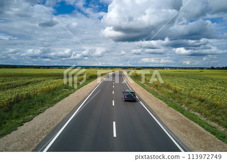 Aerial view of intercity road between green agricultural fields with fast driving car. Top view from drone of highway traffic Aerial view of intercity road between green agricultural fields with fast driving car. Top view from drone of highway traffic 113972749