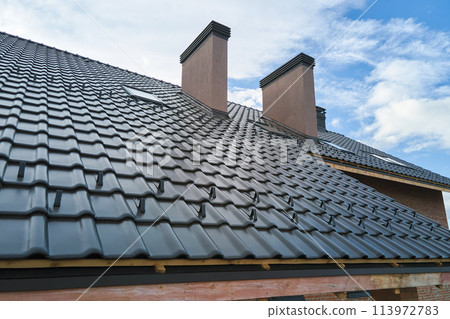 Closeup snow guard for safety in winter on house roof top covered with ceramic shingles. Tiled covering of building Closeup snow guard for safety in winter on house roof top covered with ceramic shingles. Tiled covering of building 113972783