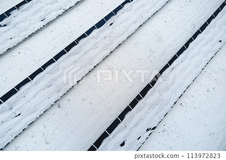 Aerial view of snow covered sustainable electric power plant with rows of solar photovoltaic panels for producing clean electrical energy. Low effectivity of renewable electricity in northern winter 113972823