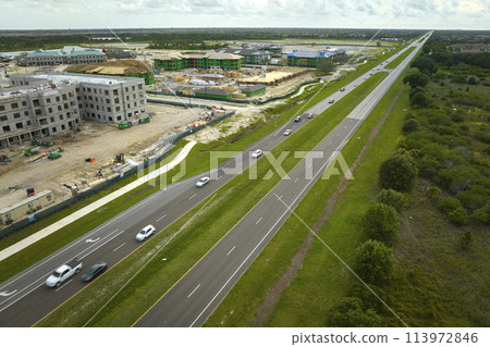 View from above of unfinished frame of apartment condos with wooden roof beams under construction. Development of residential housing near state highway in US suburbs. Real estate market in the USA 113972846