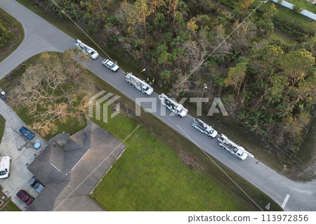 Electrician workers repairing damaged power lines using bucket trucks after hurricane in Florida residential area 113972856