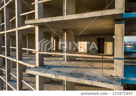 Interior of a concrete residential apartment building room with unfinished bare walls and support pillars for future walls under construction. 113972947