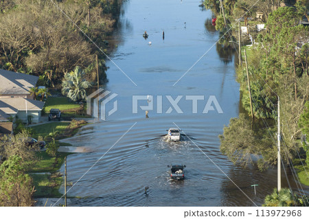 Flooded Florida road with evacuating cars and surrounded with water houses in suburban residential area. Consequences of hurricane natural disaster 113972968