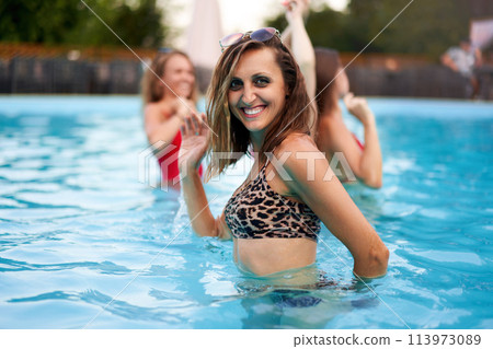 Senior woman in bikini hanging out with friends at pool party in beach club. Mature female in one piece swimwear enjoy summer. Old lady has fun swimming in water at luxury private villa swimming pool 113973089