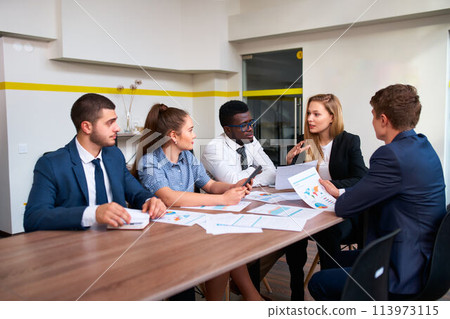 Female boss leads global business brief with multicultural team in modern office, discussing graphs. Diverse group of professionals engage in corporate strategy session, focus on growth. 113973115