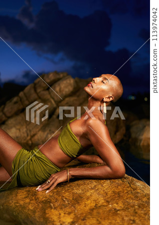 Trans sexual black fashion model in open dress, brass jewelry poses lying on big stone inside natural pool surrouded by rocks on tropical island at night. Androgynous ethnic person in backwater. Trans sexual black fashion model in open dress, brass jewelry poses lying on big stone inside natural pool surrouded by rocks on tropical island at night. Androgynous ethnic person in backwater. 113974042