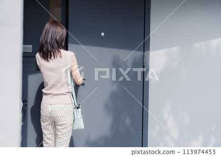 Young woman opening the front door of her house 113974453