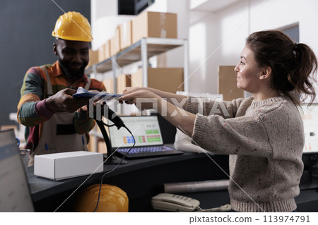 African american employee signing inventory report, discussing customers online orders before start preparing packages in warehouse. Supervisor standing at counter desk checking goods logistics 113974791