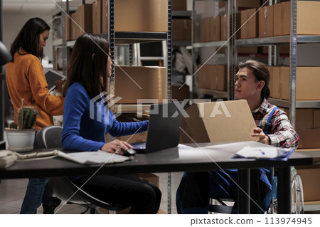 Postal service employees managing package sending and receiving operations in warehouse. Storehouse workers checking parcel packing while working in inclusive storage room 113974945