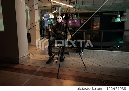 Ransomware, cyber criminal recording threat video on smartphone, asking money for ransom, calling victim. Phishing, blackmail, man scammer in mask stealing information at night time Ransomware, cyber criminal recording threat video on smartphone, asking money for ransom, calling victim. Phishing, blackmail, man scammer in mask stealing information at night time 113974988