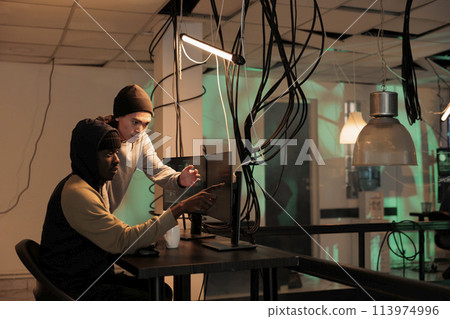 Diverse team of spies using trojan virus to ccause malware, working together to crack firewall encryption at night. Male hackers analyzing database to steal personal sensitive information. Diverse team of spies using trojan virus to ccause malware, working together to crack firewall encryption at night. Male hackers analyzing database to steal personal sensitive information. 113974996