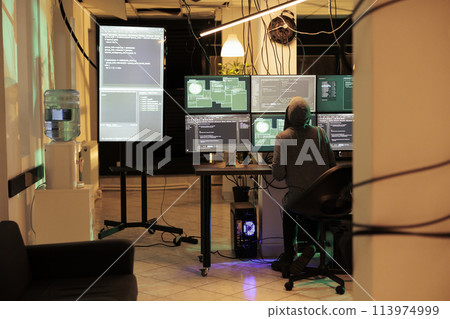 Young hacker working on multiple monitors to hack online server, cracking firewall encryption to steal passwords. Professional thief looking at screen planting trojan virus at night. Young hacker working on multiple monitors to hack online server, cracking firewall encryption to steal passwords. Professional thief looking at screen planting trojan virus at night. 113974999