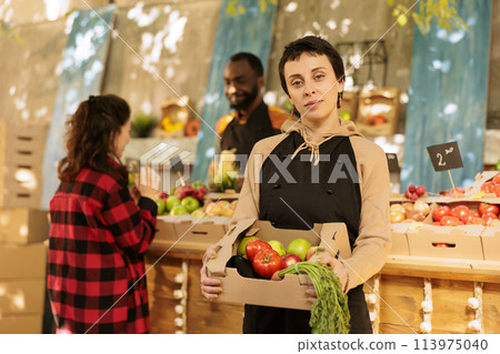 Cheerful female seller of fruits and veggies market stand owner showing fresh organic produce box and looking at camera. Ypung farmer selling healthy local produce from roadside stand, eco products. Cheerful female seller of fruits and veggies market stand owner showing fresh organic produce box and looking at camera. Ypung farmer selling healthy local produce from roadside stand, eco products. 113975040