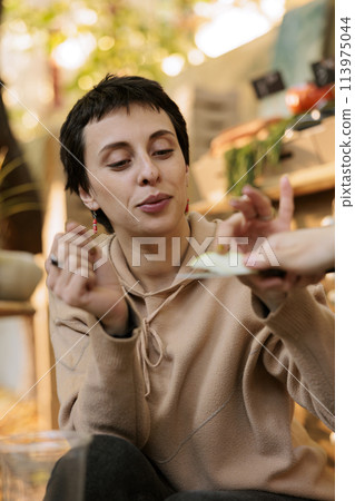 Young woman customer in selective focus, tasting fresh organic green apple while shopping at outdoor farmers market. Before purchasing, a female client samples locally grown organic fruits. Young woman customer in selective focus, tasting fresh organic green apple while shopping at outdoor farmers market. Before purchasing, a female client samples locally grown organic fruits. 113975044