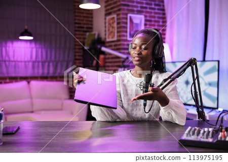 Portrait of african american tech vlogger reviewing laptop in rgb lights living room studio. Entertaining content creator filming technology channel vlog for gadget enthusiasts, presenting info Portrait of african american tech vlogger reviewing laptop in rgb lights living room studio. Entertaining content creator filming technology channel vlog for gadget enthusiasts, presenting info 113975195