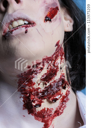 Extreme close up shot of bloody injury on woman neck acting as zombie for horror film scene. Gore undead corpse scars with fake blood achieved through professional SFX makeup for Halloween costume Extreme close up shot of bloody injury on woman neck acting as zombie for horror film scene. Gore undead corpse scars with fake blood achieved through professional SFX makeup for Halloween costume 113975209