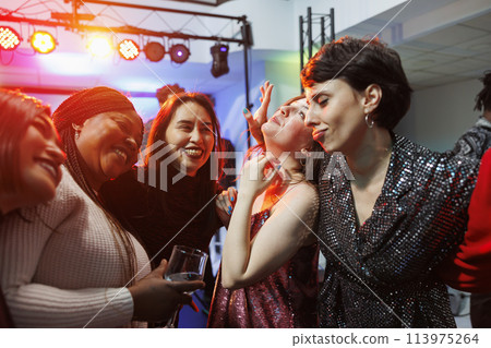 Cheerful smiling women drinking alcohol, hugging and partying together in nightclub. Carefree diverse girlfriends holding beverage glasses, laughing and having fun in club Cheerful smiling women drinking alcohol, hugging and partying together in nightclub. Carefree diverse girlfriends holding beverage glasses, laughing and having fun in club 113975264