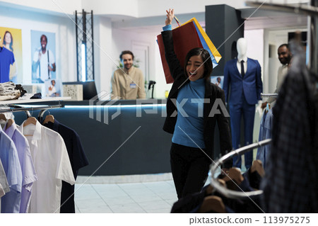 Happy woman making dance moves with shopping bags after buying garment in clothing store. Fashion boutique smiling asian customer raising hand with paper packages of purchases 113975275