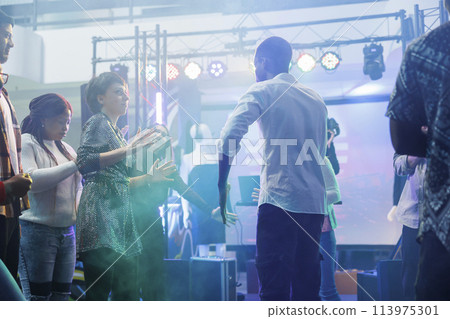 Man and woman friends showing fun moves at dance battle while partying in nightclub. Dancers improvising on dancefloor illuminated with colorful lights while celebrating in club 113975301