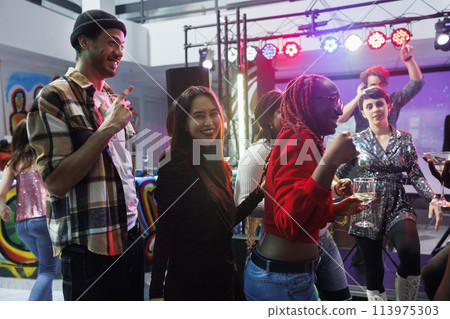 Carefree smiling people drinking alcohol beverage and having fun at disco party in nightclub. Cheerful young friends celebrating and enjoying nightlife leisure activity in club 113975303