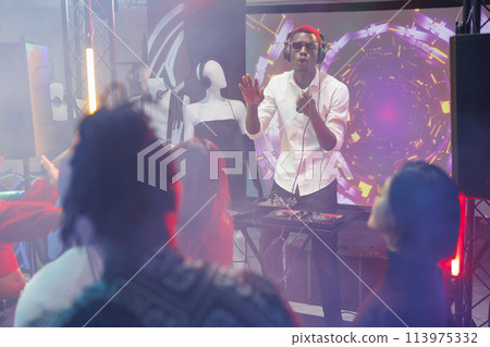 Dj playing on stage while people having fun at disco party in nightclub. Young african american man performing electronic music for clubbers crowd at discotheque in club with spotlights 113975332