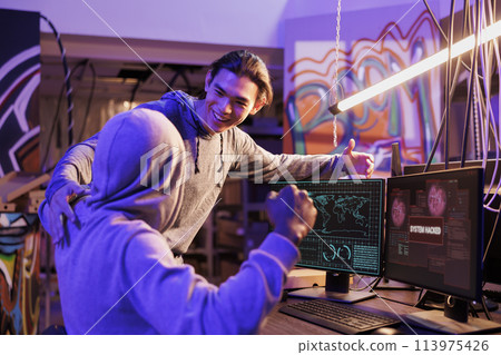 Successful criminals gaining unauthorized access to computer network and celebrating with victory gesture. Happy internet scammers getting system hacked message on screen Successful criminals gaining unauthorized access to computer network and celebrating with victory gesture. Happy internet scammers getting system hacked message on screen 113975426