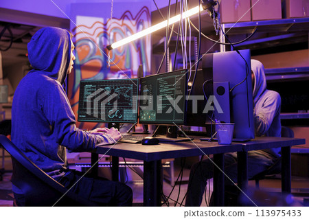 Hackers committing internet crime while breaking into server and stealing privacy information. Cybercriminals planning phishing and doing online scam on computer in dark room hideout Hackers committing internet crime while breaking into server and stealing privacy information. Cybercriminals planning phishing and doing online scam on computer in dark room hideout 113975433