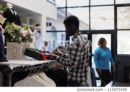 African american customer looking at shelf full with accessories, checking fashionable belt in modern boutique. Stylish man shopping for casual wear in clothing store. Fashion concept African american customer looking at shelf full with accessories, checking fashionable belt in modern boutique. Stylish man shopping for casual wear in clothing store. Fashion concept 113975489
