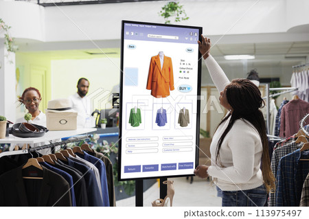 Female customer reviewing clothes to purchase from self ordering kiosk service, looking at trendy fashion items on touch screen board. Young client checking products on monitor. 113975497