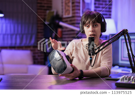 Portrait of tech vlogger reviewing VR goggles in rgb lights living room studio. Entertaining content creator filming technology channel vlog for gadget enthusiasts using professional camera and mic Portrait of tech vlogger reviewing VR goggles in rgb lights living room studio. Entertaining content creator filming technology channel vlog for gadget enthusiasts using professional camera and mic 113975525