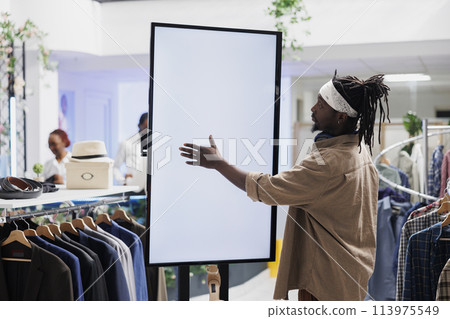 Customer using empty white smart screen to browse clothes in store. African american stylish man touching interactive blank display while shopping for apparel in mall boutique 113975549