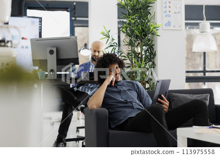 Start up business company manager watching video on digital tablet during break in office. Arab young entrepreneur browsing social media and relaxing on couch in coworking space Start up business company manager watching video on digital tablet during break in office. Arab young entrepreneur browsing social media and relaxing on couch in coworking space 113975558