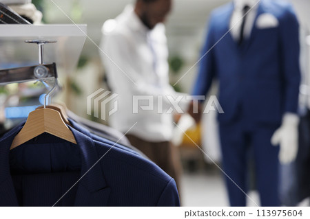Apparel hanging on rack in shopping mall clothing section with blurred background. Male stylish jackets on hangers showcasing merchandise new collection in fashion boutique Apparel hanging on rack in shopping mall clothing section with blurred background. Male stylish jackets on hangers showcasing merchandise new collection in fashion boutique 113975604