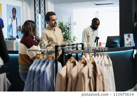 Man assistant helping woman choosing clothes in shopping mall fashion boutique. Clothing store worker customer asking worker for advice while selecting outfit in showroom Man assistant helping woman choosing clothes in shopping mall fashion boutique. Clothing store worker customer asking worker for advice while selecting outfit in showroom 113975614