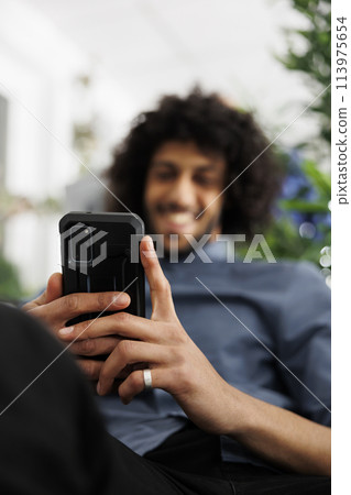 Smiling business company employee browsing social network on mobile phone in office. Relaxed arab executive manager surfing internet and chatting online on smartphone at work break Smiling business company employee browsing social network on mobile phone in office. Relaxed arab executive manager surfing internet and chatting online on smartphone at work break 113975654