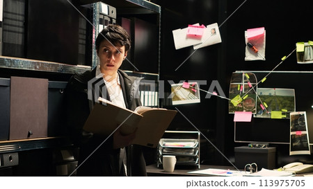 Detective conducting crime investigation with case files and forensic evidence in police agency office, law enforcement. Professional inspector evaluating evidence authenticity, illegal records. Detective conducting crime investigation with case files and forensic evidence in police agency office, law enforcement. Professional inspector evaluating evidence authenticity, illegal records. 113975705
