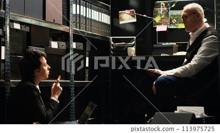 Law enforcement commitment to solve case. Two police officers working under pressure to discover new incriminating proof and help in catching culprit, detective work. Handheld shot. 113975725