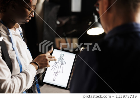 Creative skilled fashion designer showing atelier shop manager graphic design sketch drawing of wedding dress she is working on. Apprentice and master manufacturing bespoke sartorial outfit Creative skilled fashion designer showing atelier shop manager graphic design sketch drawing of wedding dress she is working on. Apprentice and master manufacturing bespoke sartorial outfit 113975739