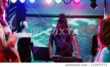 Funky adult mixing beats at club, having fun on stage audio equipment and partying. Young DJ working with sounds station dancing with people at discotheque event. Handheld shot. Funky adult mixing beats at club, having fun on stage audio equipment and partying. Young DJ working with sounds station dancing with people at discotheque event. Handheld shot. 113975771