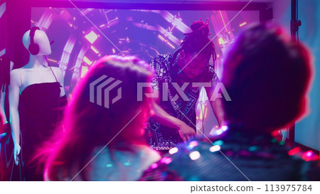 Cool man using DJ mixing station at club, creating funky music beats for crowd of people in discotheque. Men and women having fun dancing with disco lights and live sound. Handheld shot. 113975784