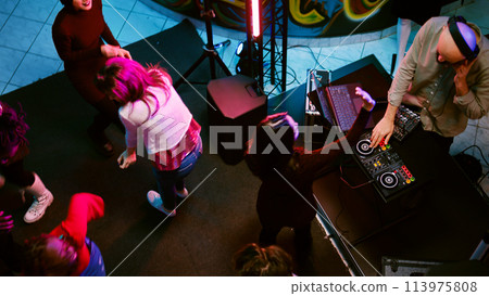 Happy persons having fun on dance floor with DJ music mix, partying with spotlights and audio performance. Group of people dancing and clubbing with electronic funky beats. Handheld shot. Happy persons having fun on dance floor with DJ music mix, partying with spotlights and audio performance. Group of people dancing and clubbing with electronic funky beats. Handheld shot. 113975808