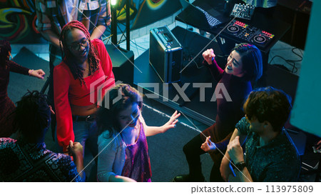 Cheerful persons doing dance moves at club, partying together on the dance floor. Modern crowd of people listening to music and dancing, having fun at nightclub for entertainment. Handheld shot. 113975809