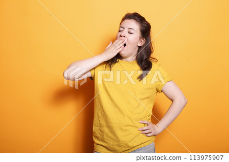 Portrait of caucasian woman yawning and covering her mouth, feeling sleepy in studio. Tired female person falling asleep while posing and standing over isolated background. Portrait of caucasian woman yawning and covering her mouth, feeling sleepy in studio. Tired female person falling asleep while posing and standing over isolated background. 113975907