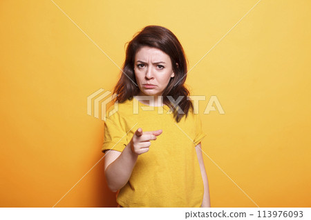 Displeased woman with serious expression points her finger at the camera. Standing over isolated background, dissatisfied person who is upset and irritated makes frustrated and angry gesture. Displeased woman with serious expression points her finger at the camera. Standing over isolated background, dissatisfied person who is upset and irritated makes frustrated and angry gesture. 113976093