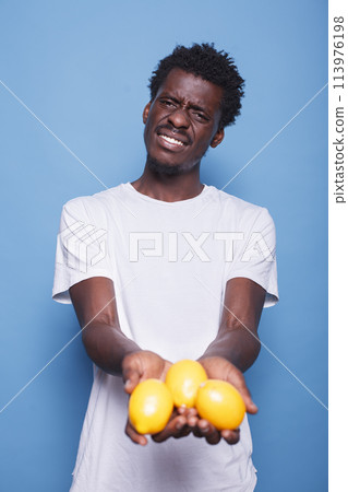African american person holding lemons for healthy vegetarian diet. Man presenting yellow citrus fruits in hands for natural nutrition with vitamins. Adult showing fresh juicy fruits to camera. African american person holding lemons for healthy vegetarian diet. Man presenting yellow citrus fruits in hands for natural nutrition with vitamins. Adult showing fresh juicy fruits to camera. 113976198