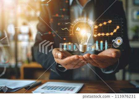 Businessman holds a glowing light bulb with digital graphics symbolizing growth and ideas 113976231