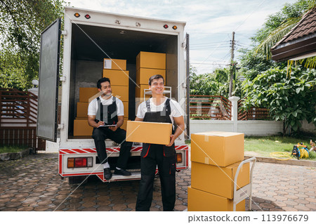 Workers unload cardboard boxes from a van. Movers work together in a relocation service. Cooperation among colleagues. Smiling employees carrying orders. relocation cooperation Moving Day Workers unload cardboard boxes from a van. Movers work together in a relocation service. Cooperation among colleagues. Smiling employees carrying orders. relocation cooperation Moving Day 113976679